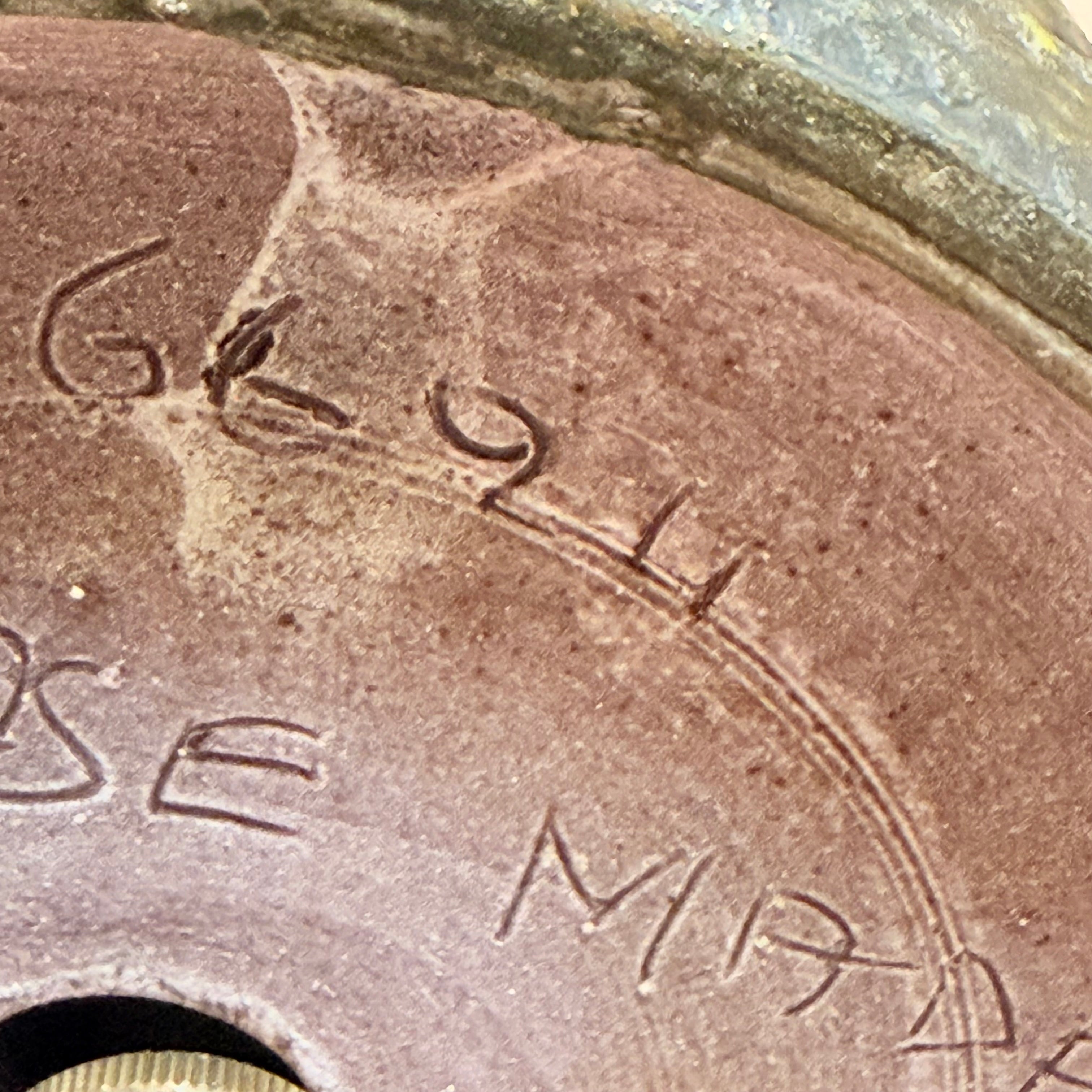Close-up of a terracotta-colored ceramic pot or planter with hand-painted markings and the words 'ROSE MIRADA' visible on the side.