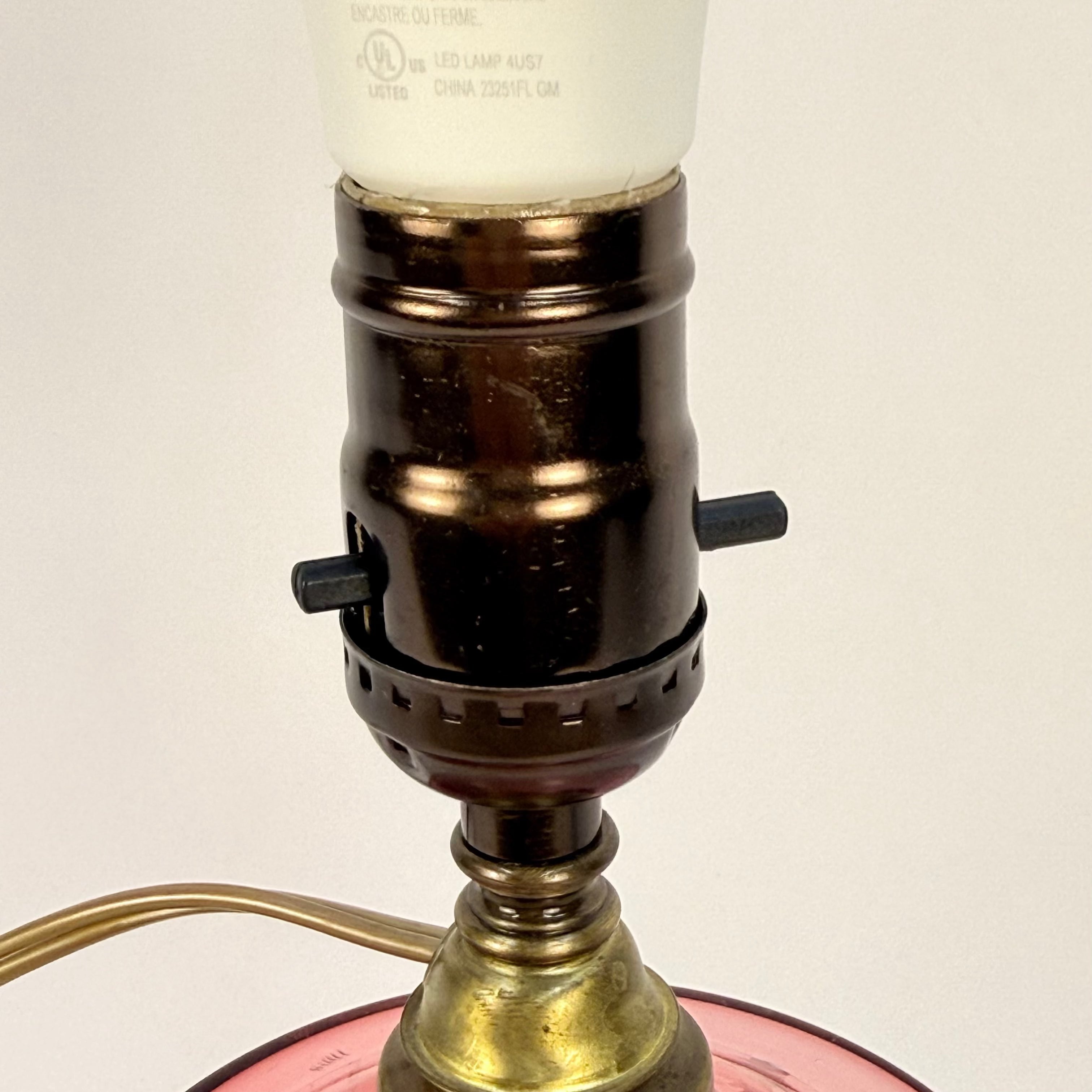 Close-up of a vintage-style lamp with a brass base and pink glass shade on a plain background.