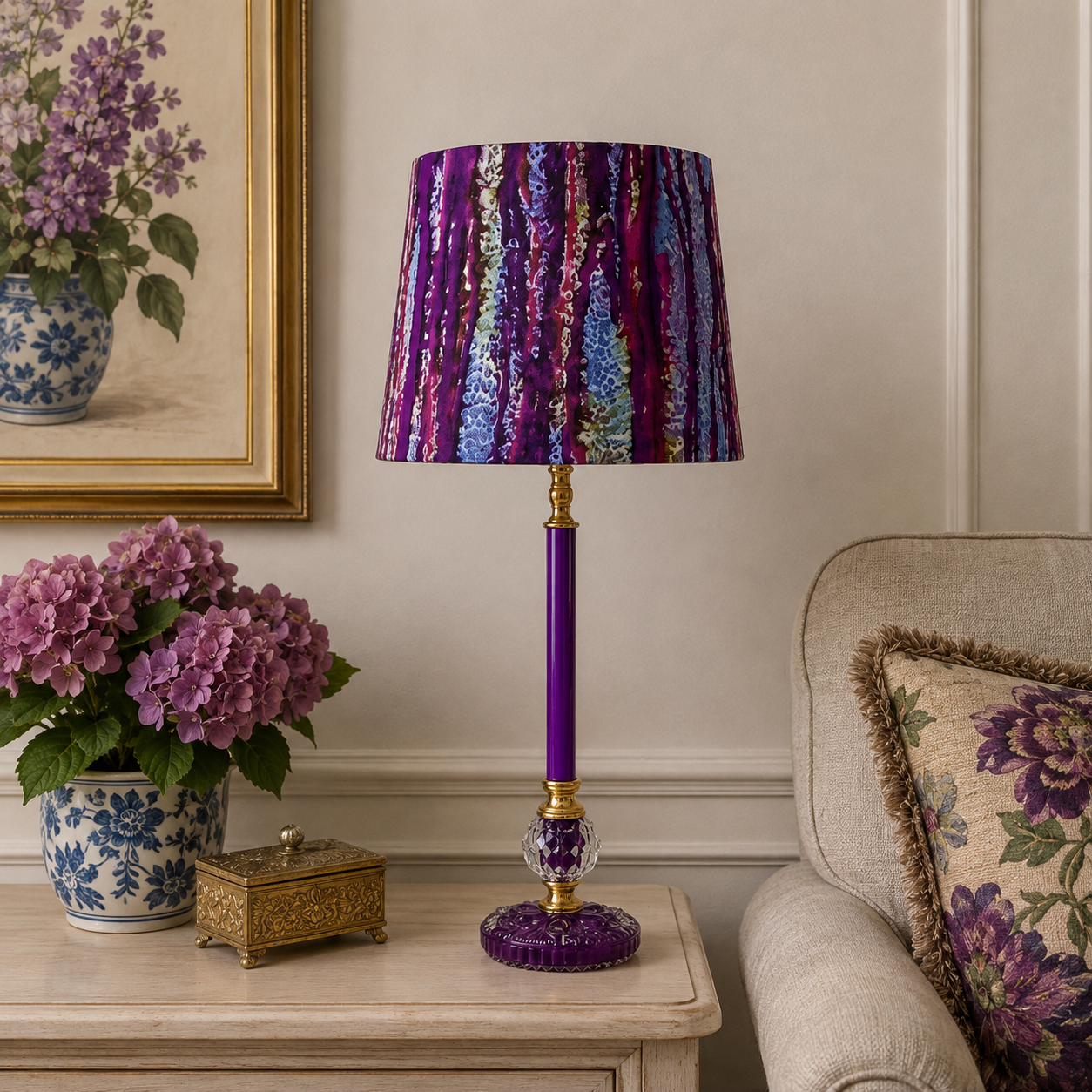 A purple table lamp with a textured, vertically striped purple, blue, and pink shade, a solid purple stem, and gold-toned metal accents, styled on a beige side table in a cozy living room setting.