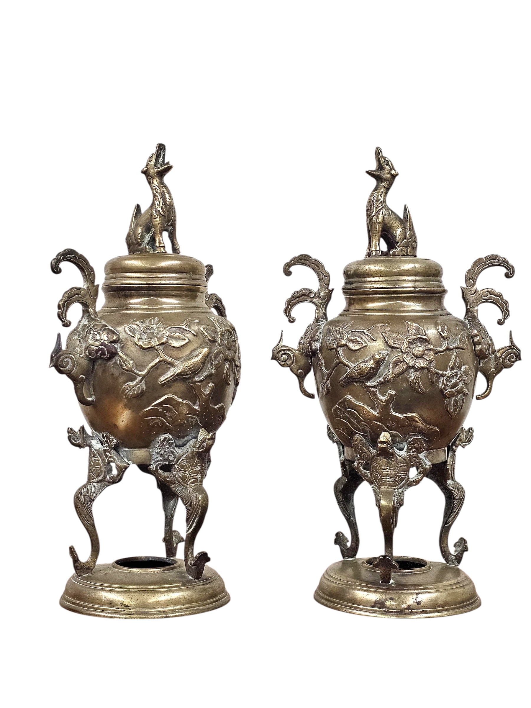 A pair of ornate antique-style metal urns with sculpted animal figures on the lids and legs, floral relief details on the bodies, and curved side handles, shown against a plain white background.