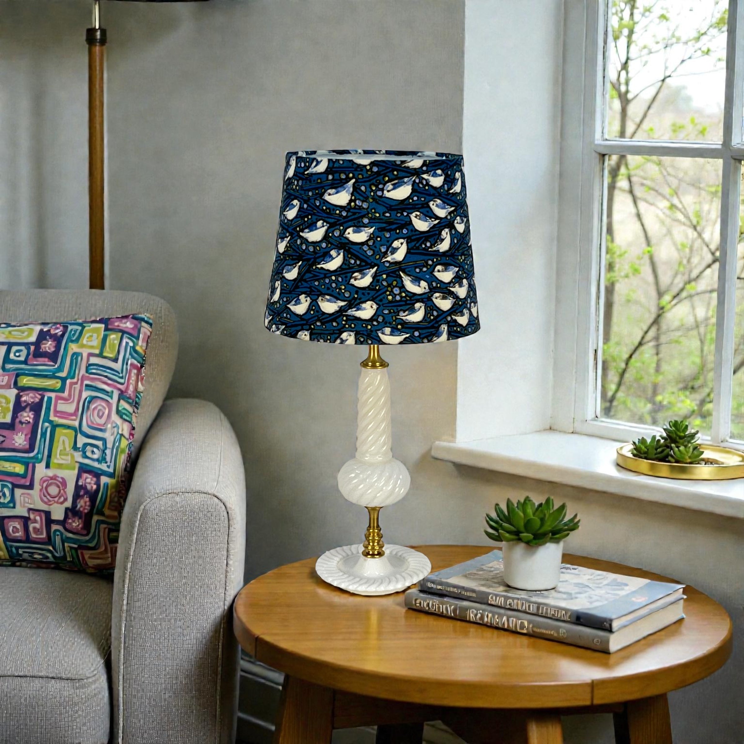 Lamp with a patterned shade on a wooden table next to a sofa with a colorful pillow.
