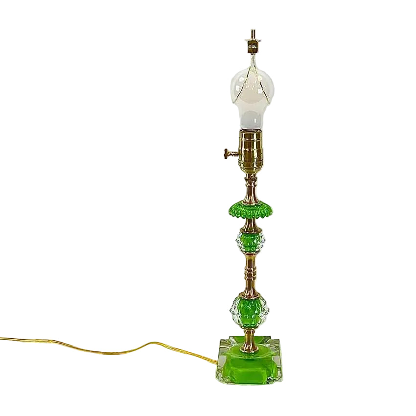 A vintage-style table lamp with a green glass base and decorative green glass accents, featuring a brass-toned metal stem and a clear glass bulb, shown on a white background with its cord extending to the left.
