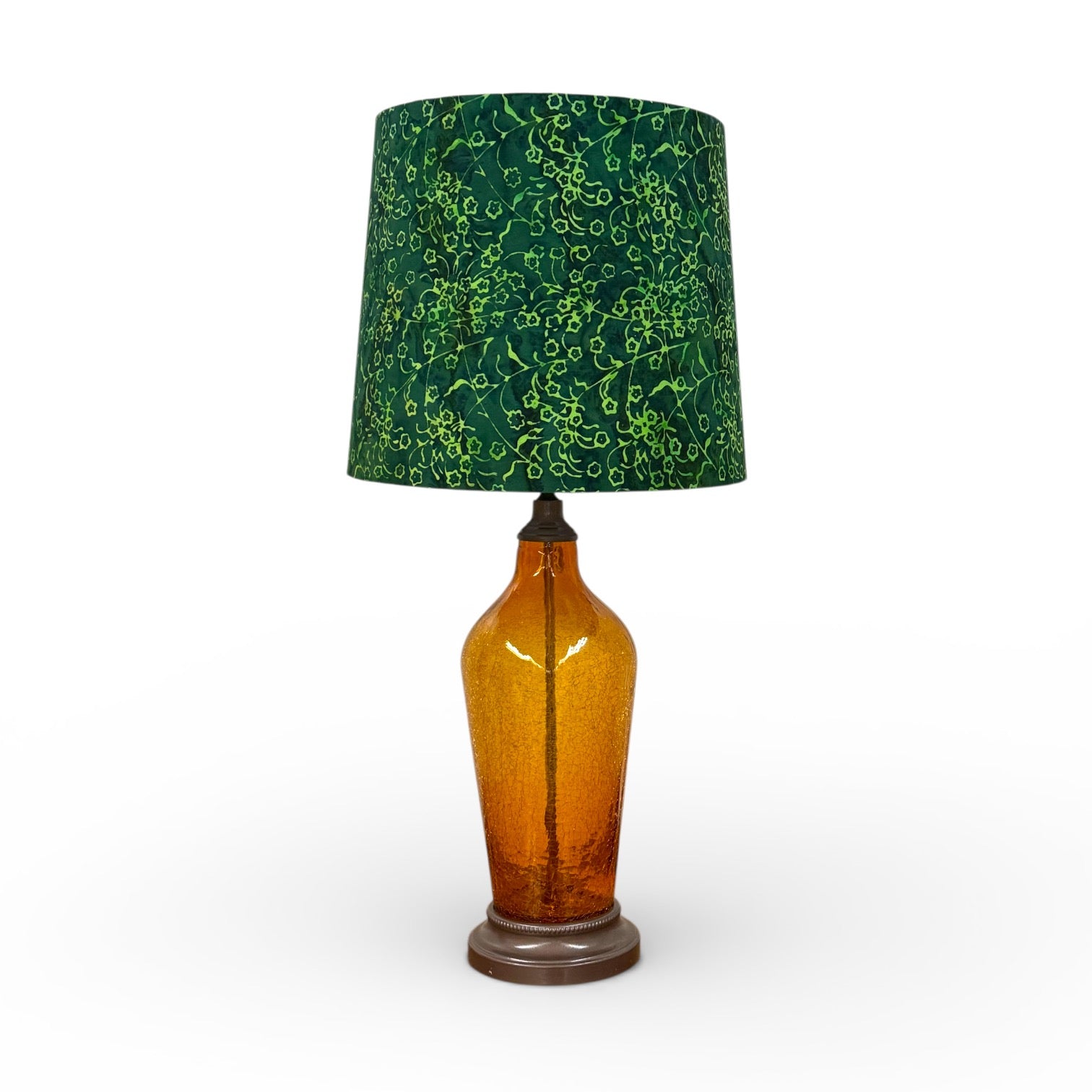 Lamp with a green patterned shade and amber glass base on a white background