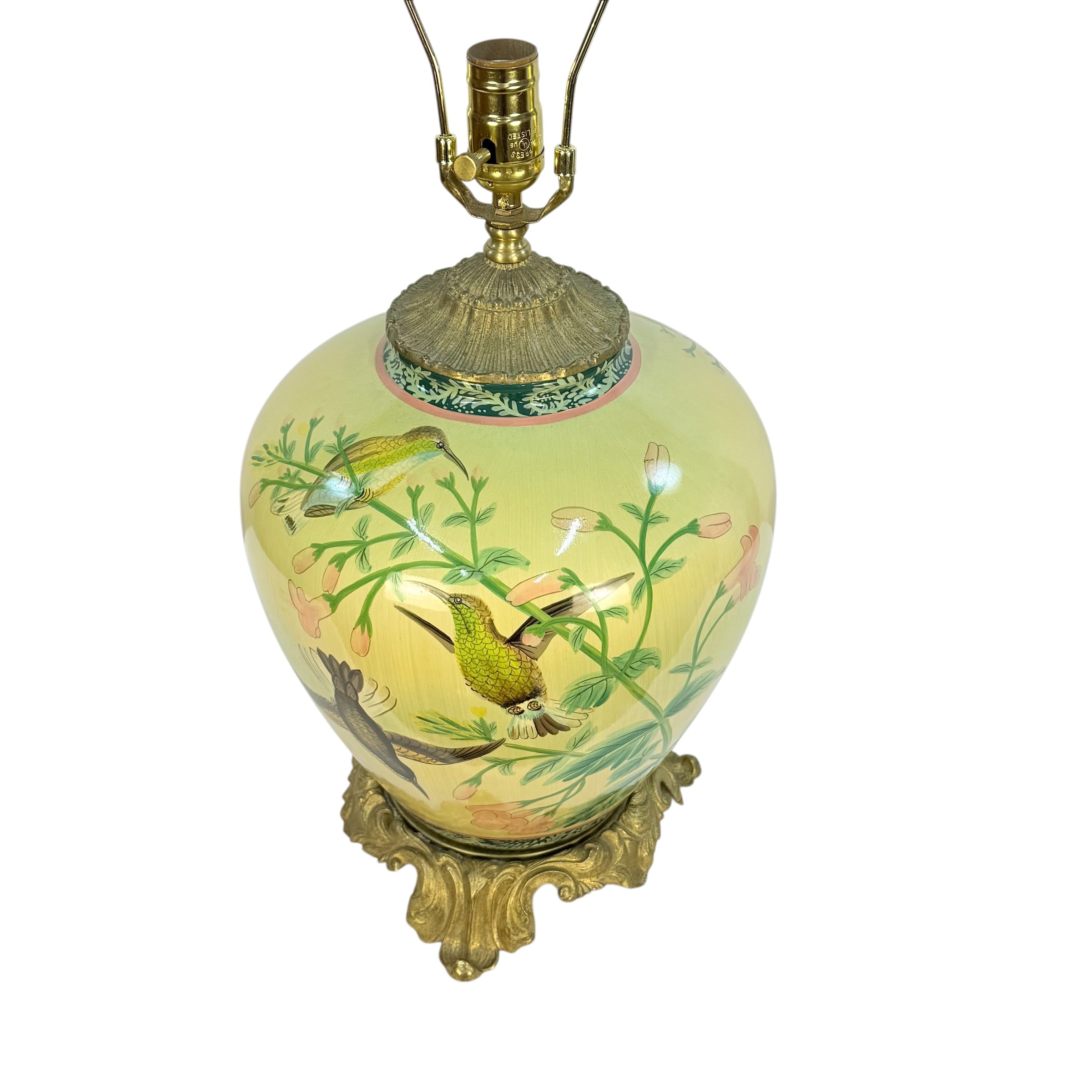 A vintage-style table lamp with a pale yellow-green ceramic vase decorated with hand-painted green birds and floral motifs, topped with an ornate gold-toned metal cap and matching lampstand.