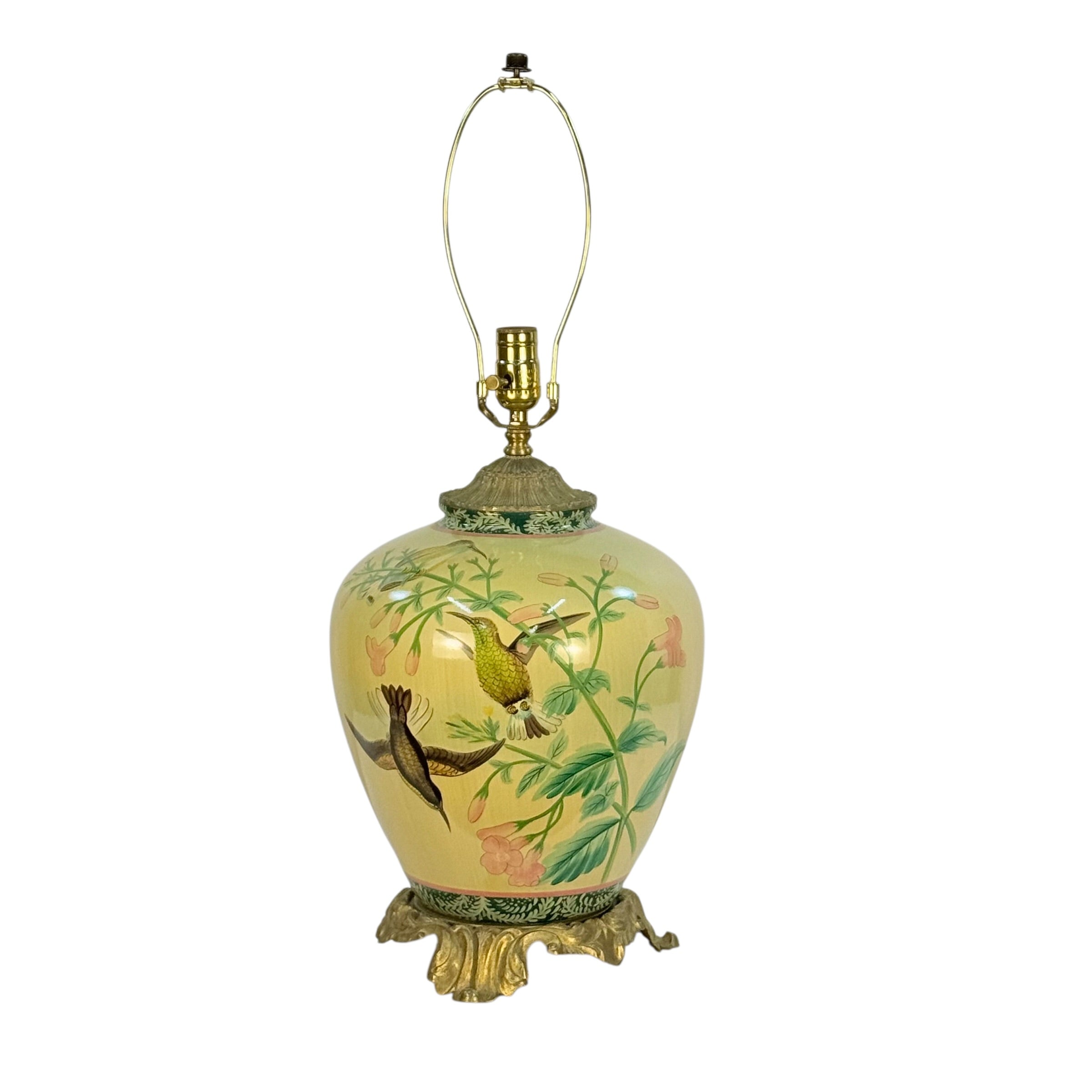 A vintage-style ceramic table lamp with a pale yellow body decorated with hand-painted birds and foliage, topped with a gold-toned metal neck and base.