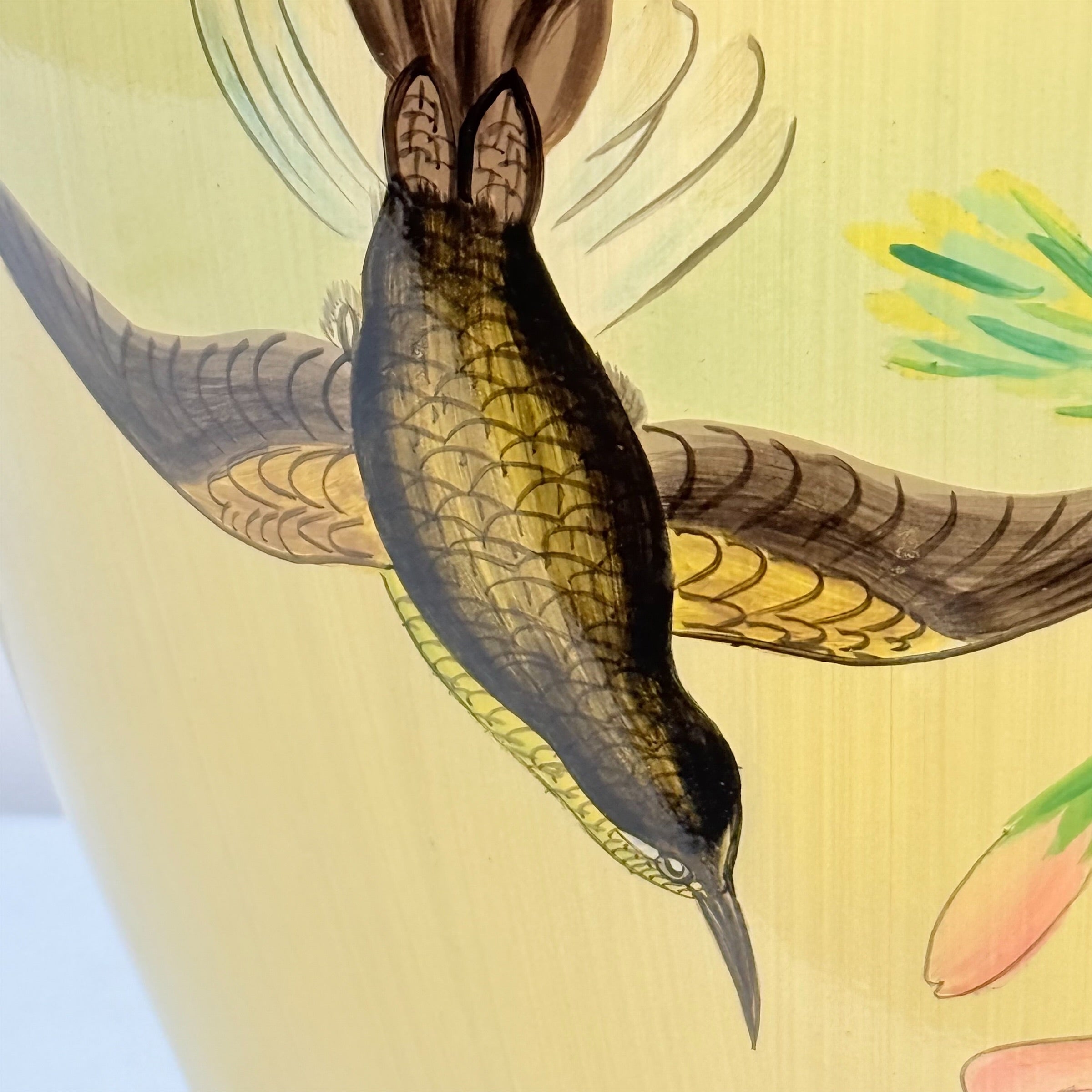 Close-up of a hand-painted ceramic vase featuring a hummingbird in flight with detailed brown, black, and gold feathering, set against a pale yellow background with floral accents.