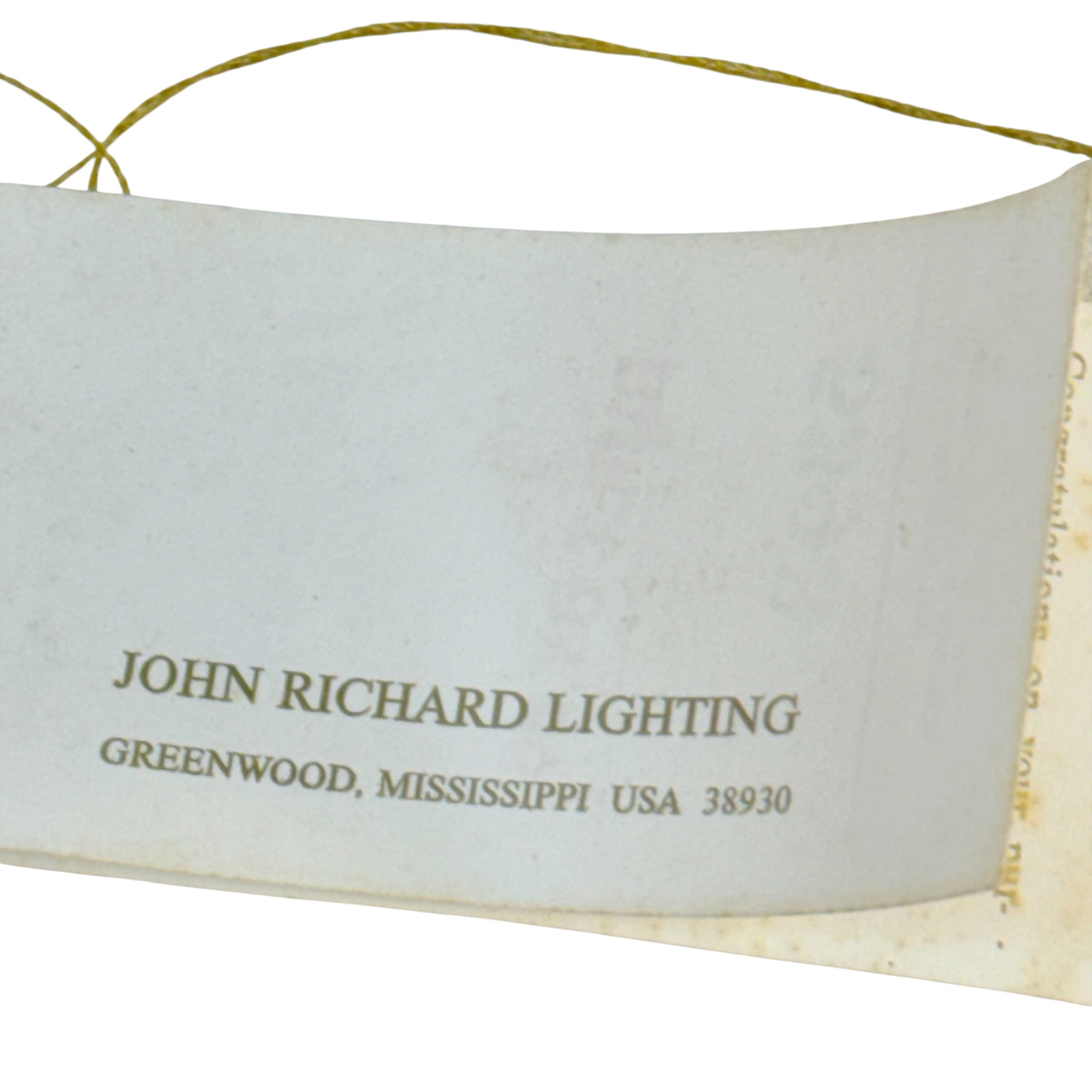 A close-up of a vintage paper tag or label for John Richard Lighting, Greenwood, Mississippi, USA, printed in brown text on an off-white background with a gold-colored string attached at the top.
