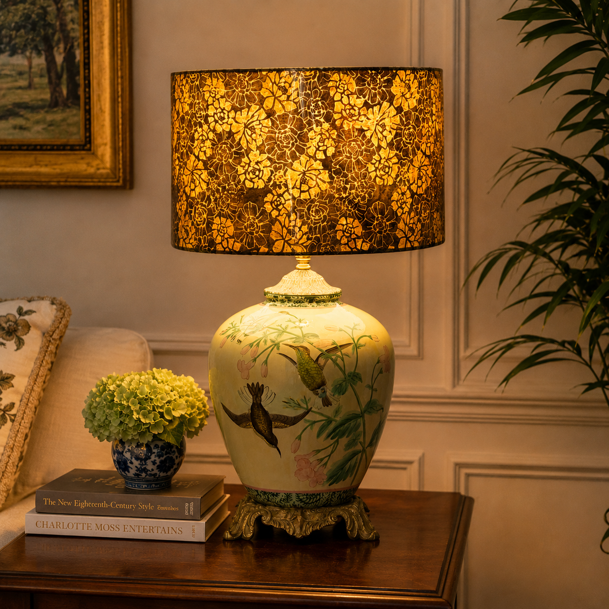 A decorative table lamp with a large drum shade and a ceramic body, styled on a wooden side table in a warm, elegant room setting.