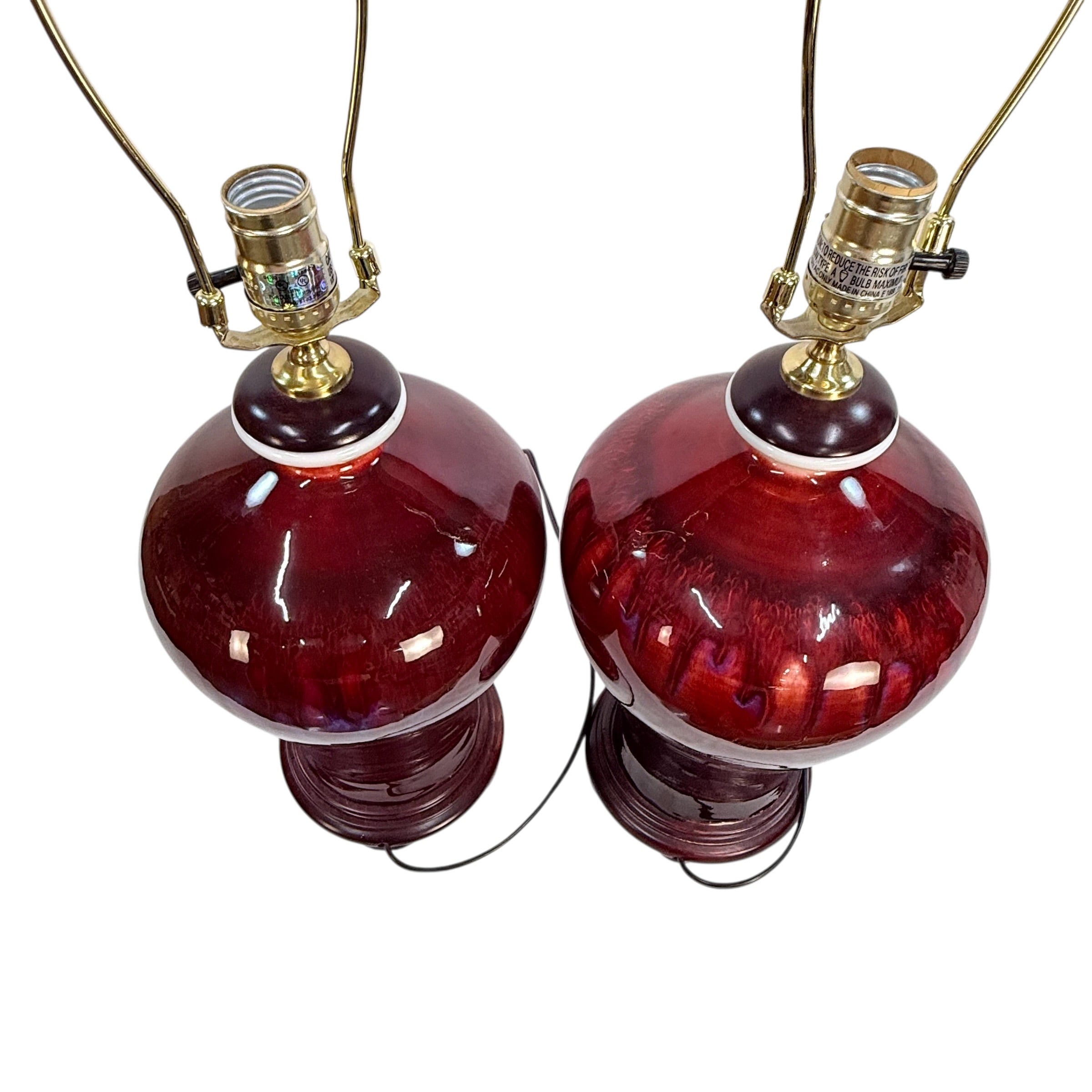 A pair of vintage table lamps with glossy dark red glass globes and brass-colored metal shades and cords, shown against a plain white background.