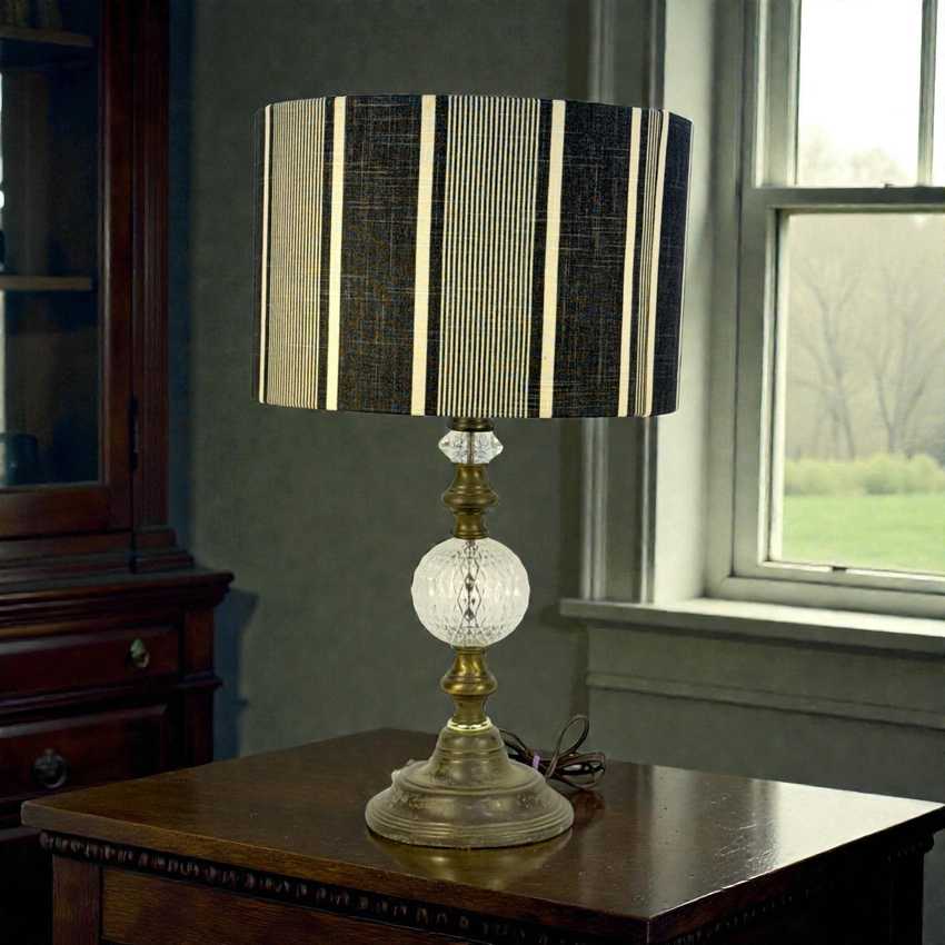 Decorative table lamp with striped shade on a wooden surface near a window.
