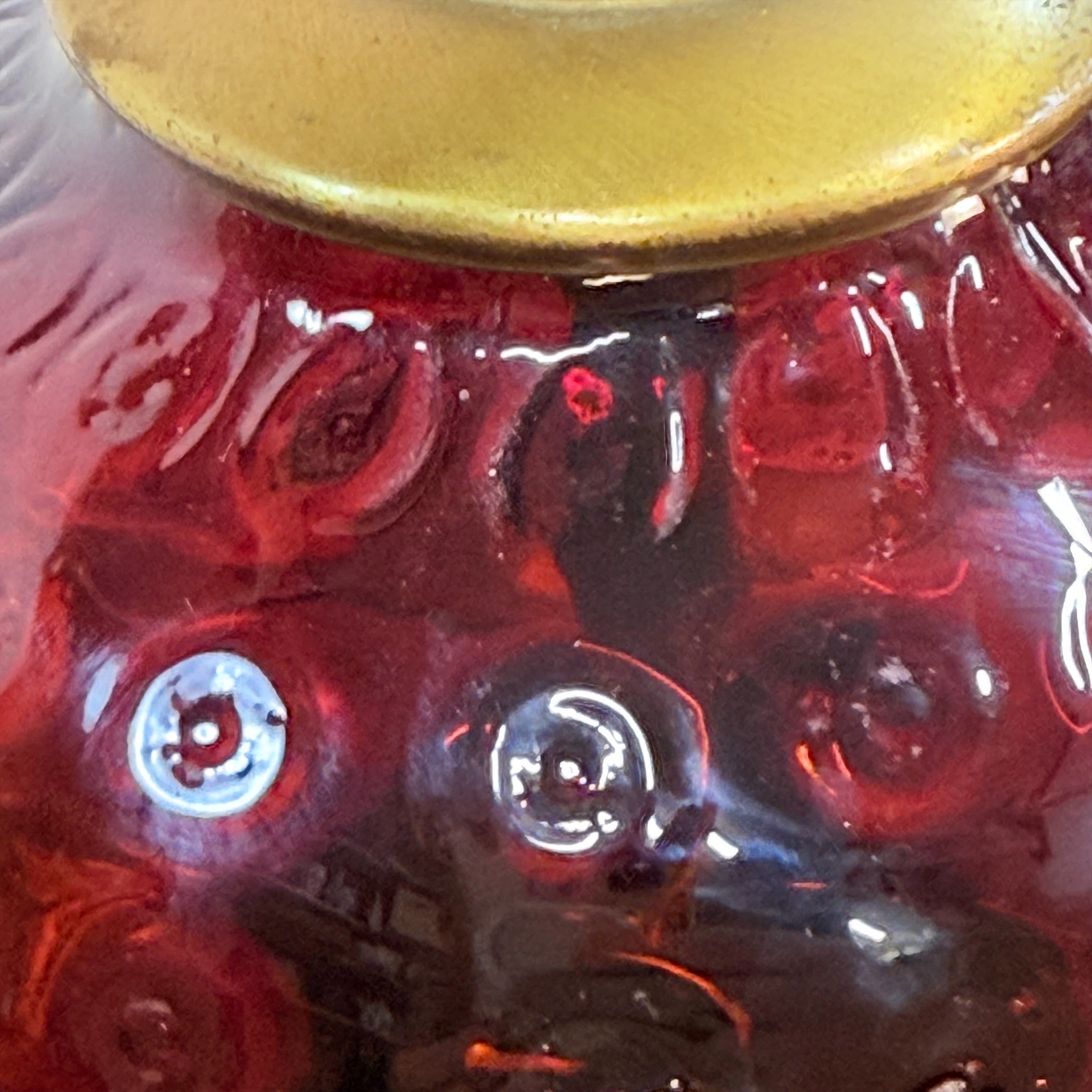 Close-up of a glossy red glass vessel with embossed circular texture and a gold-toned rim at the top.