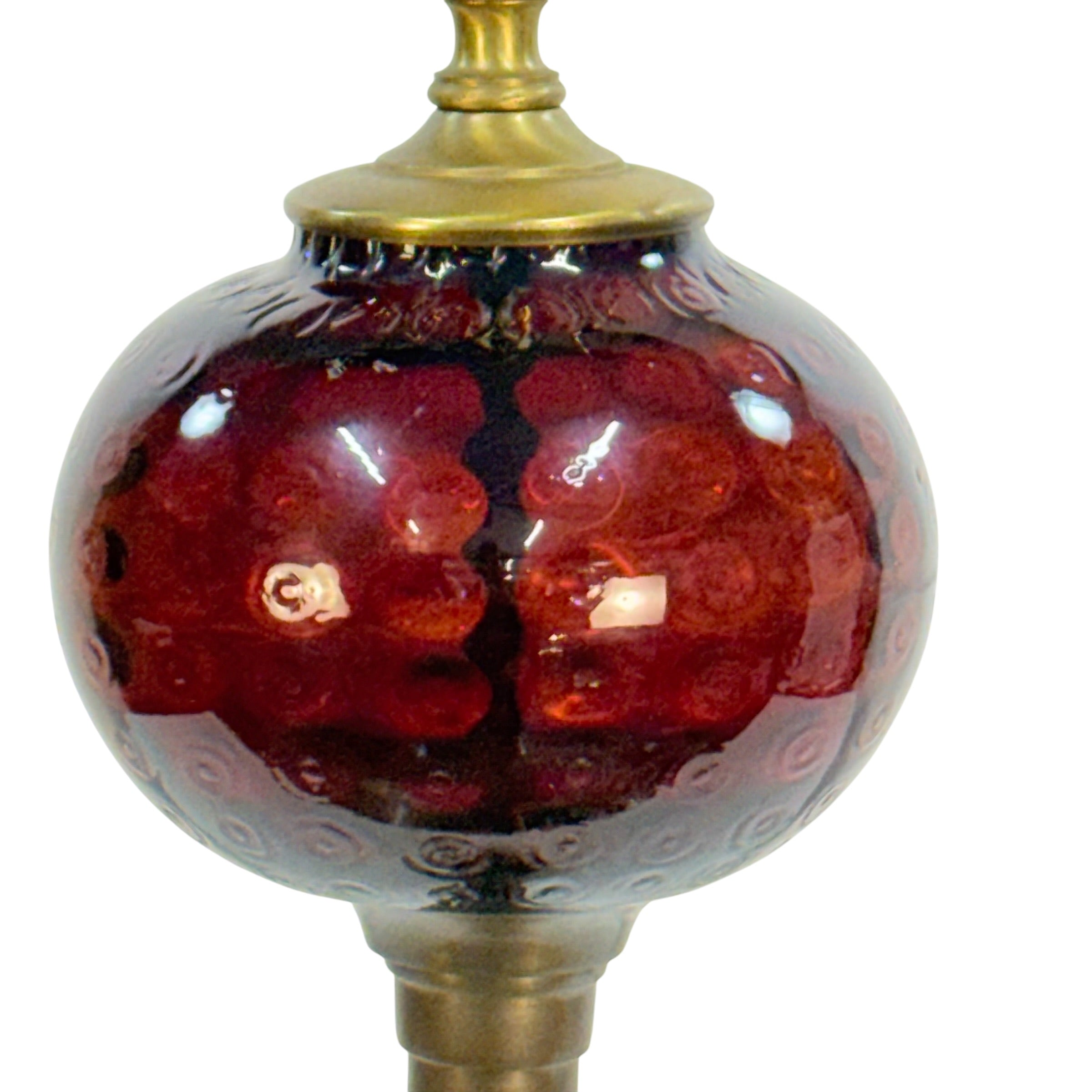 A close-up of a decorative glass lamp shade or orb with a glossy deep red and amber marbled pattern, topped and supported by a brass-toned metal finial.