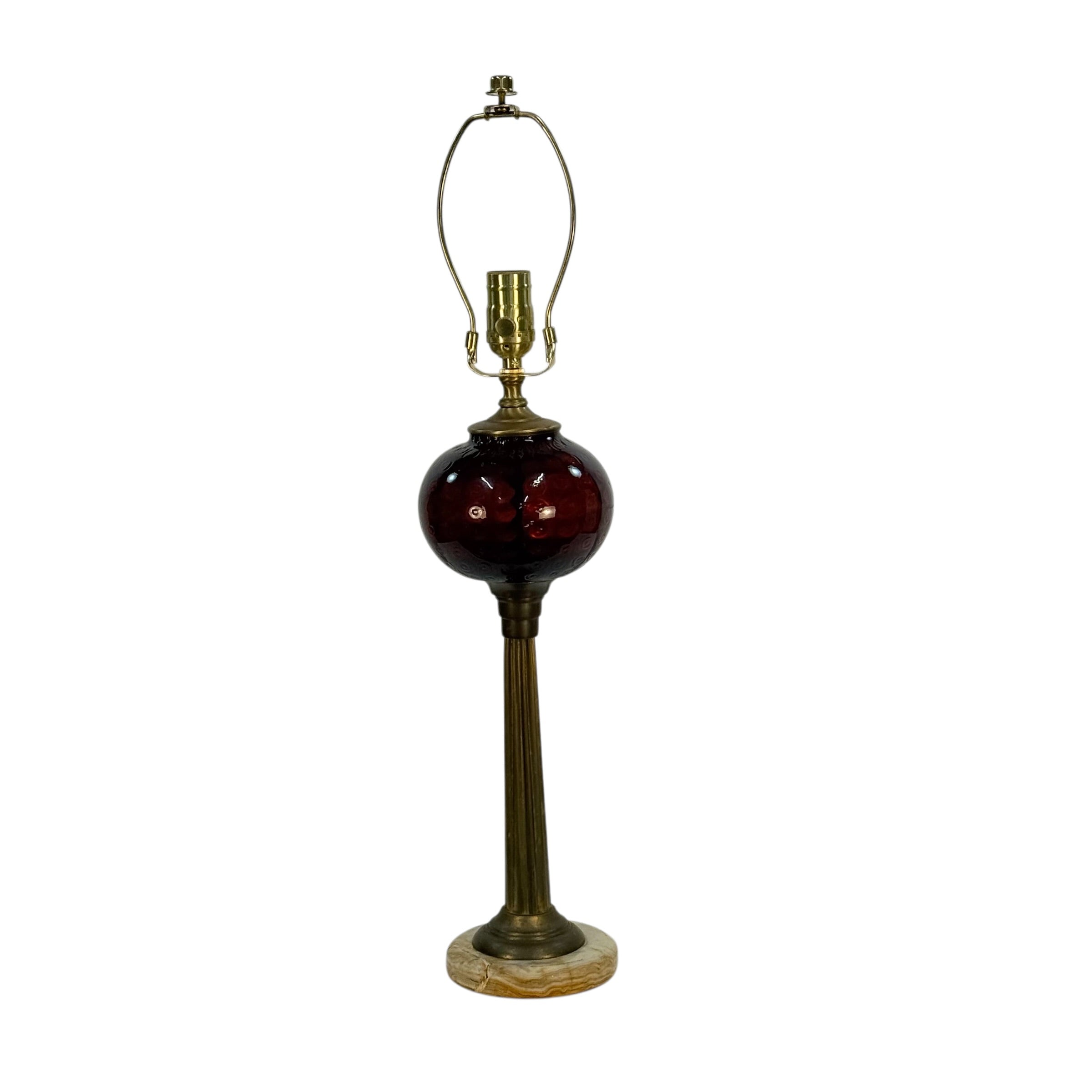 A vintage-style table lamp featuring a deep burgundy glass globe shade, a fluted brass stem, a matching brass arched shade support, and a round marble base, shown against a plain white background.