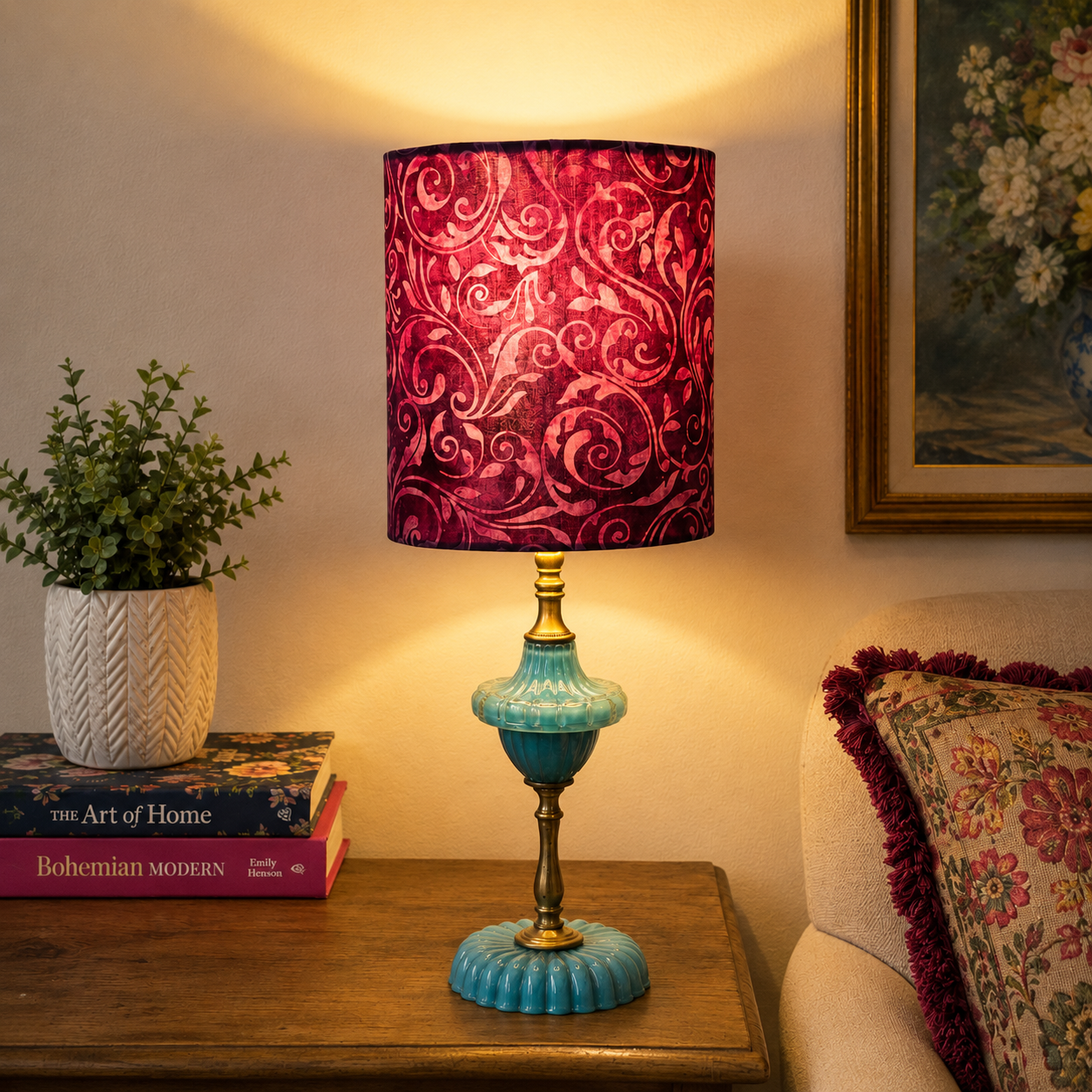 A table lamp with a deep magenta and burgundy patterned fabric shade and a turquoise blue ceramic base with brass accents, styled on a wooden side table in a cozy room setting.