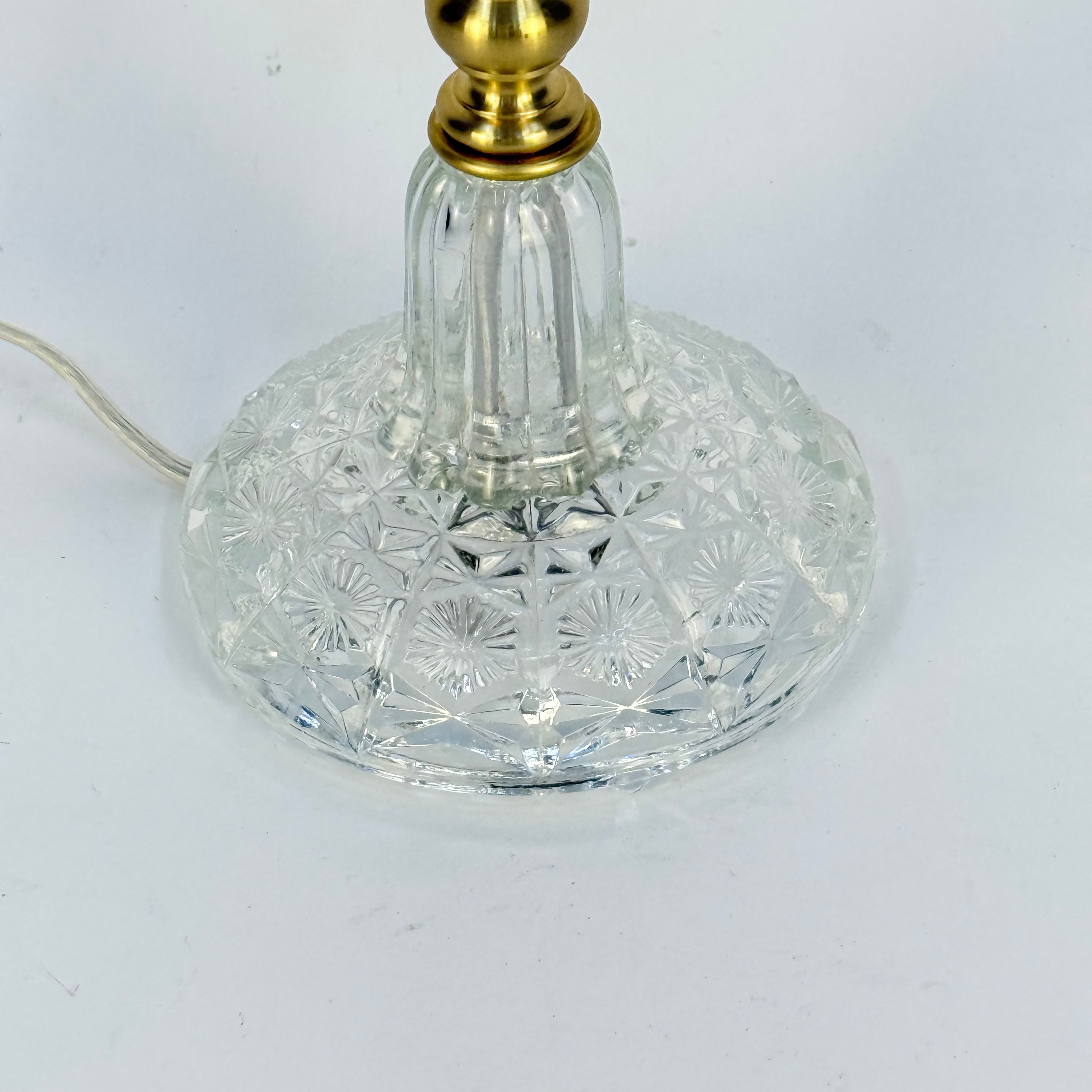 Clear glass lamp base with gold fixture on a white background