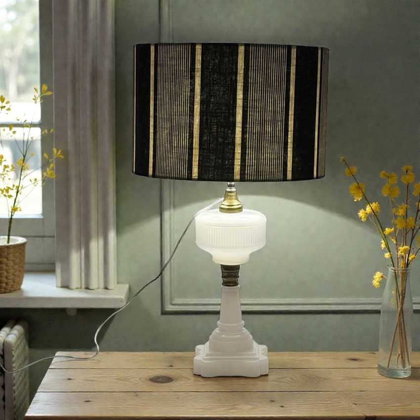 Table lamp with a black and gold striped shade on a wooden table, with a vase of yellow flowers in the background.