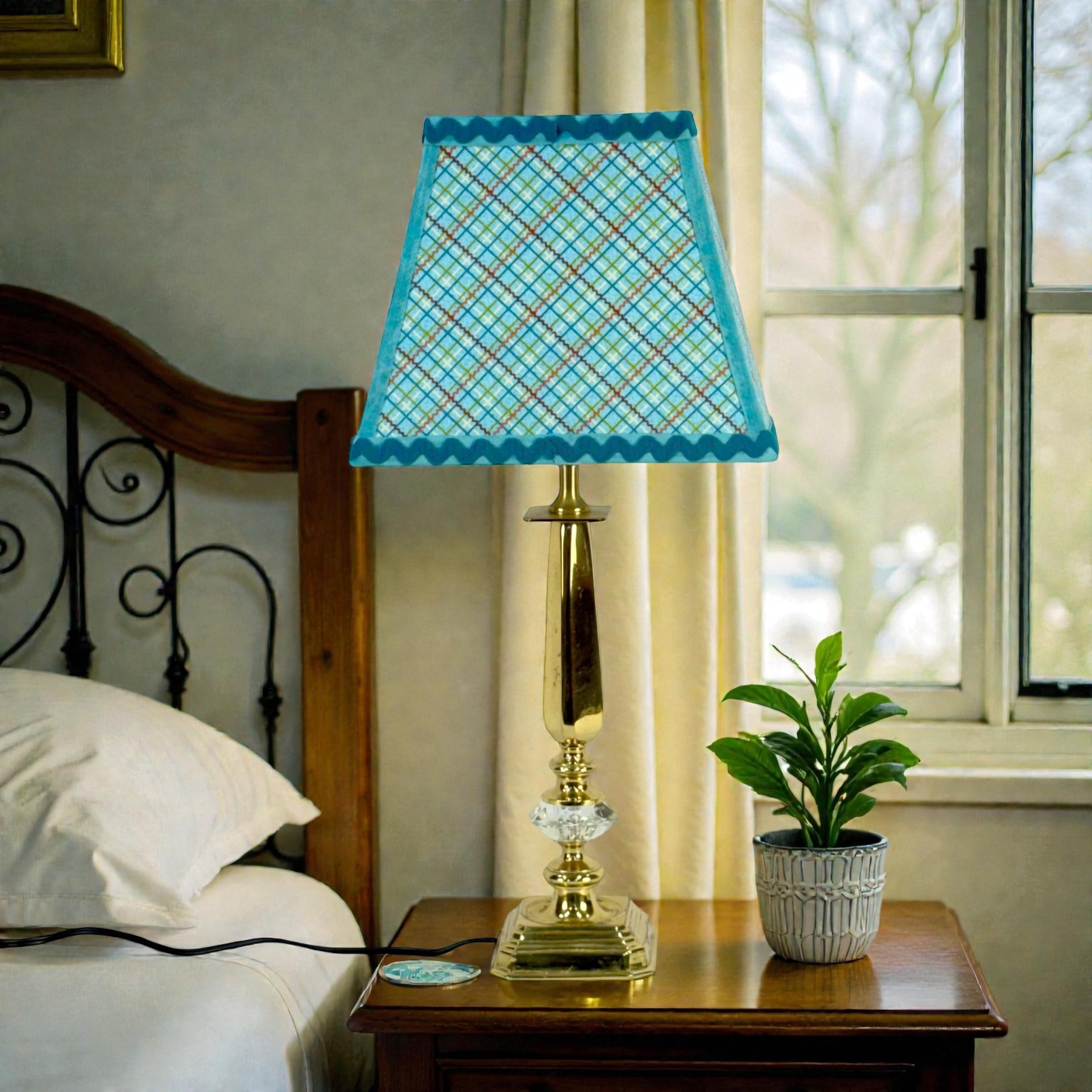 Table lamp with a blue checkered shade on a wooden nightstand next to a bed.