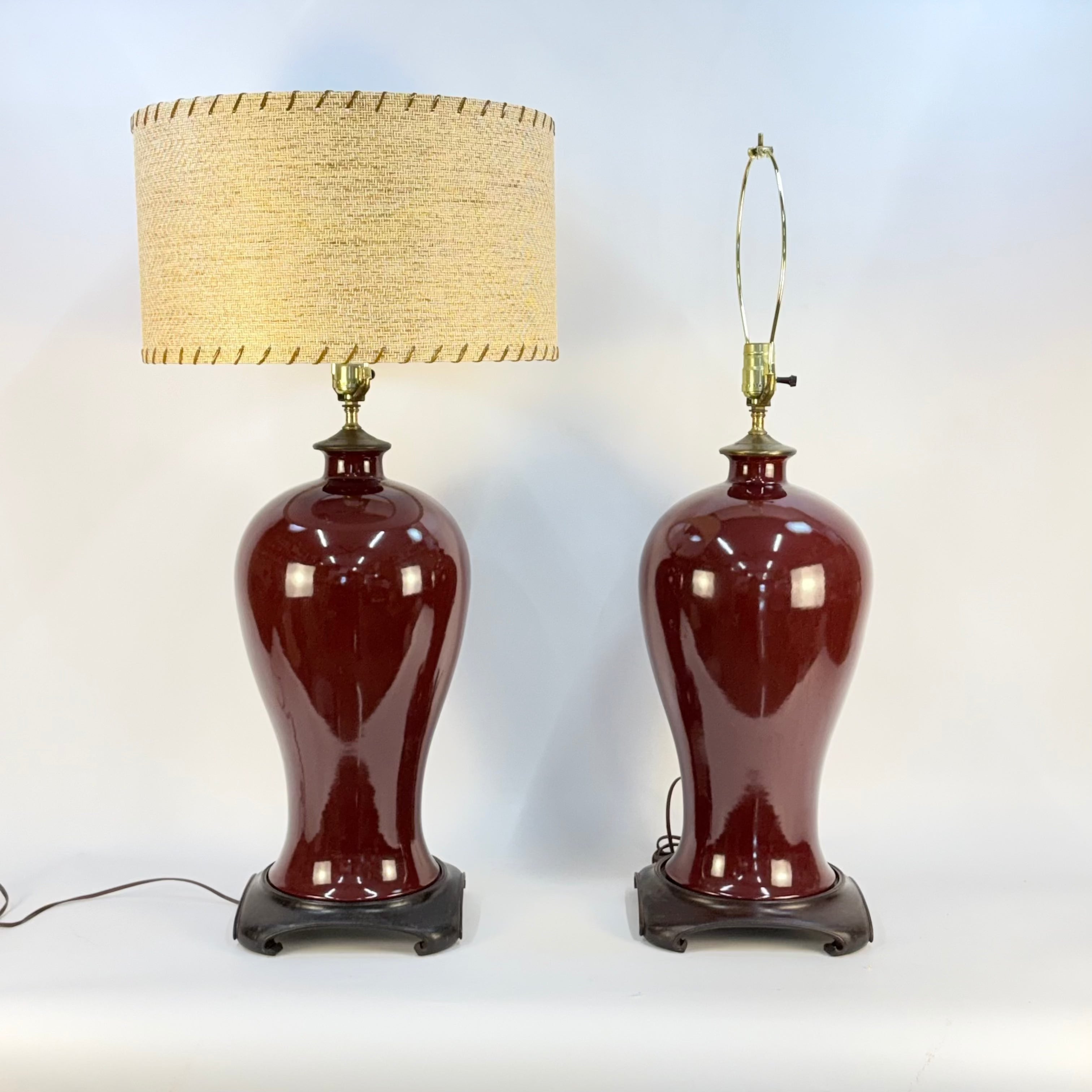Two red ceramic table lamps with beige lampshades on a white background