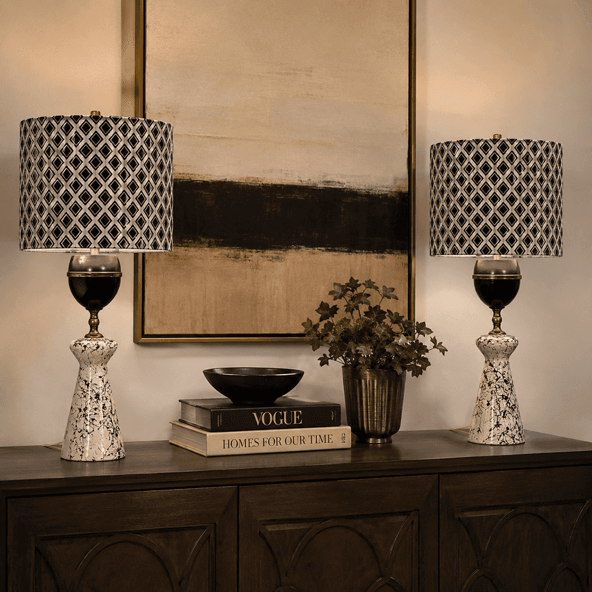 Two matching table lamps with black-and-white patterned drum shades and ornate white bases, displayed on a dark wood console in a styled interior setting.
