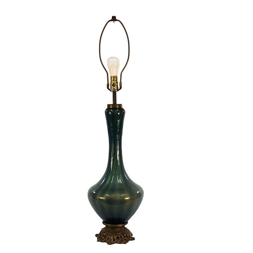 A vintage-style table lamp with a glossy dark green to teal glass vase-shaped base, an ornate bronze-colored metal pedestal foot, and a matching arched metal shade frame holding a clear bulb, shown against a plain white background.