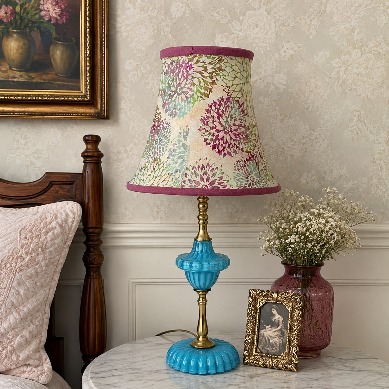 A decorative table lamp with a cream floral lampshade, purple trim, and a turquoise blue ribbed glass base with gold-toned metal accents, styled on a marble nightstand in a bedroom setting.