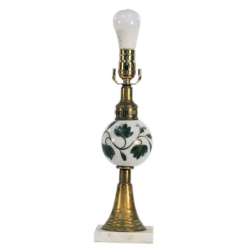 A vintage-style table lamp featuring a white glass globe with a green floral pattern, a brass neck and base, and a white glass bulb, set on a white marble base against a white background.