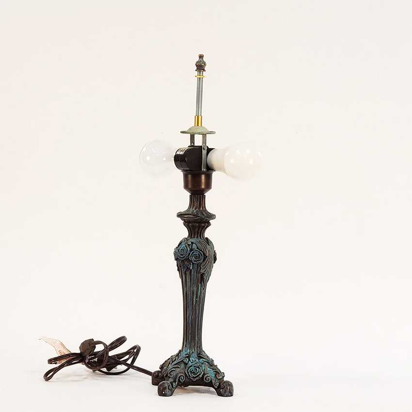 An ornate table lamp with a dark bronze and turquoise-blue distressed metal base, featuring two white globe bulbs in a swivel mount and a visible power cord on a white background.