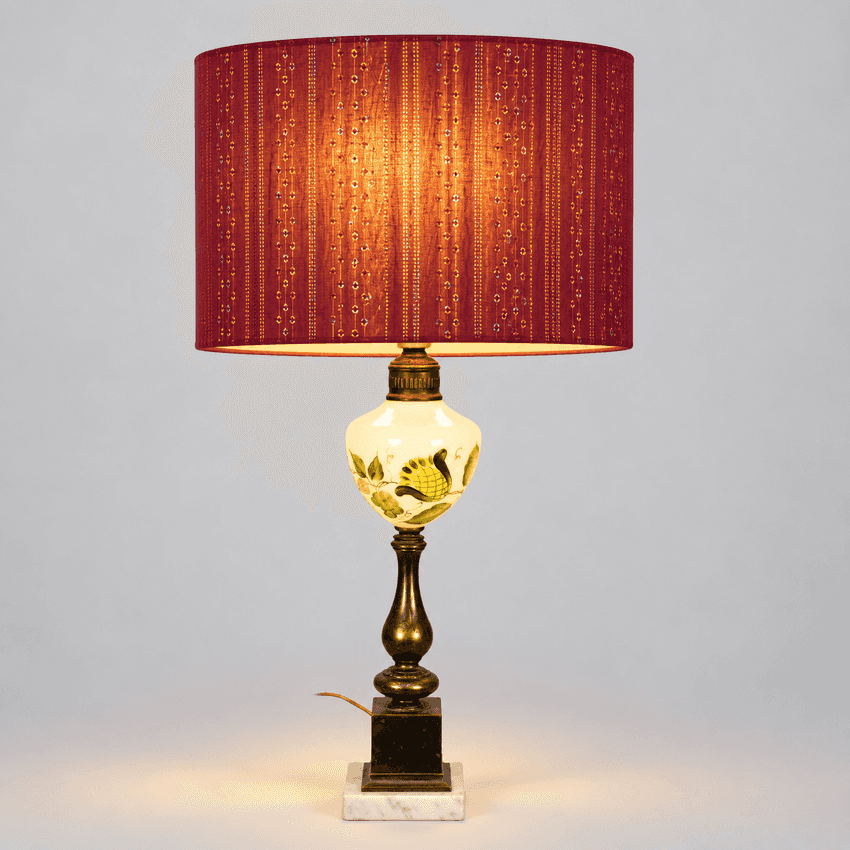 A table lamp with a red patterned fabric shade, a white glass globe decorated with a yellow sunflower, and a brass-toned metal stem on a square base.