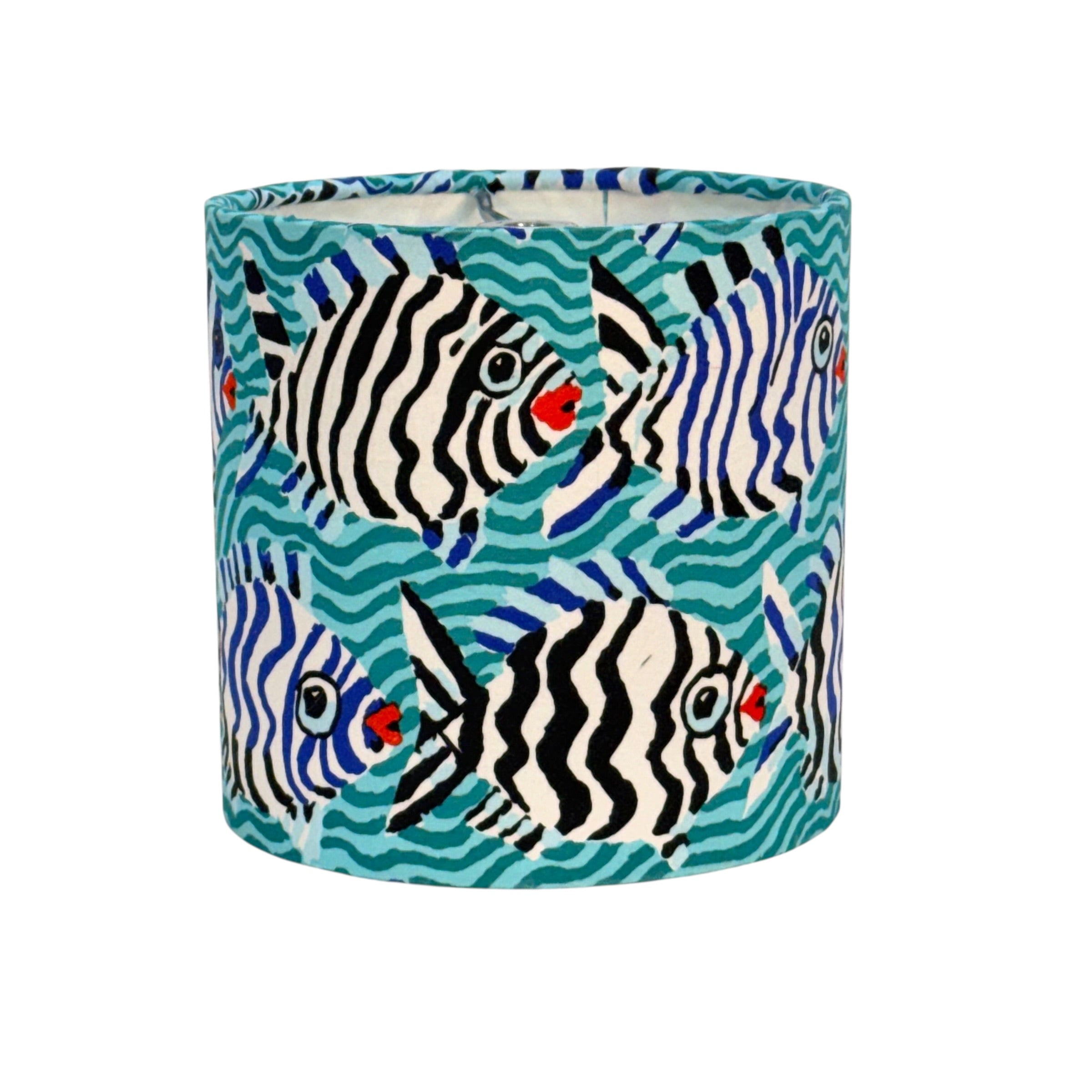 A cylindrical drum lampshade featuring a vibrant tropical print of black and white striped fish swimming over teal and blue wavy water, isolated on a white background.