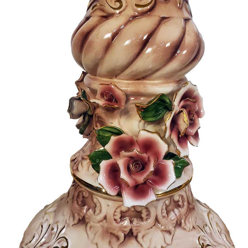 Close-up of an ornate ceramic vase or decorative vessel with a sculpted floral neck. The piece features glossy pink and white roses with green leaves and gold accents, set against a plain white background.