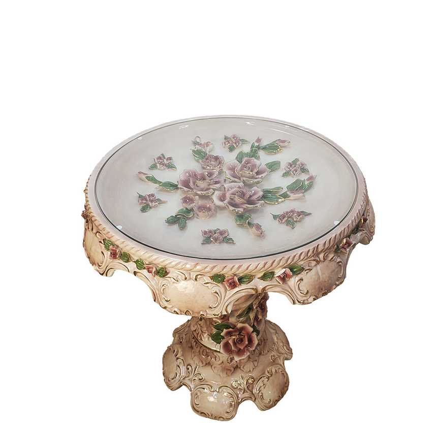 An ornate pedestal side table with a round glass top decorated with pink roses and green leaves, set on a carved beige stone base.
