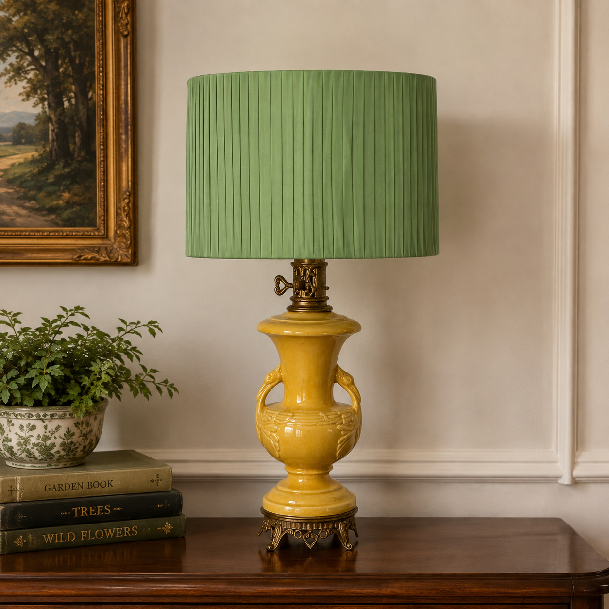 A yellow ceramic table lamp with a pleated sage green drum shade, displayed on a dark wood console table in a styled room setting next to a potted plant and books.