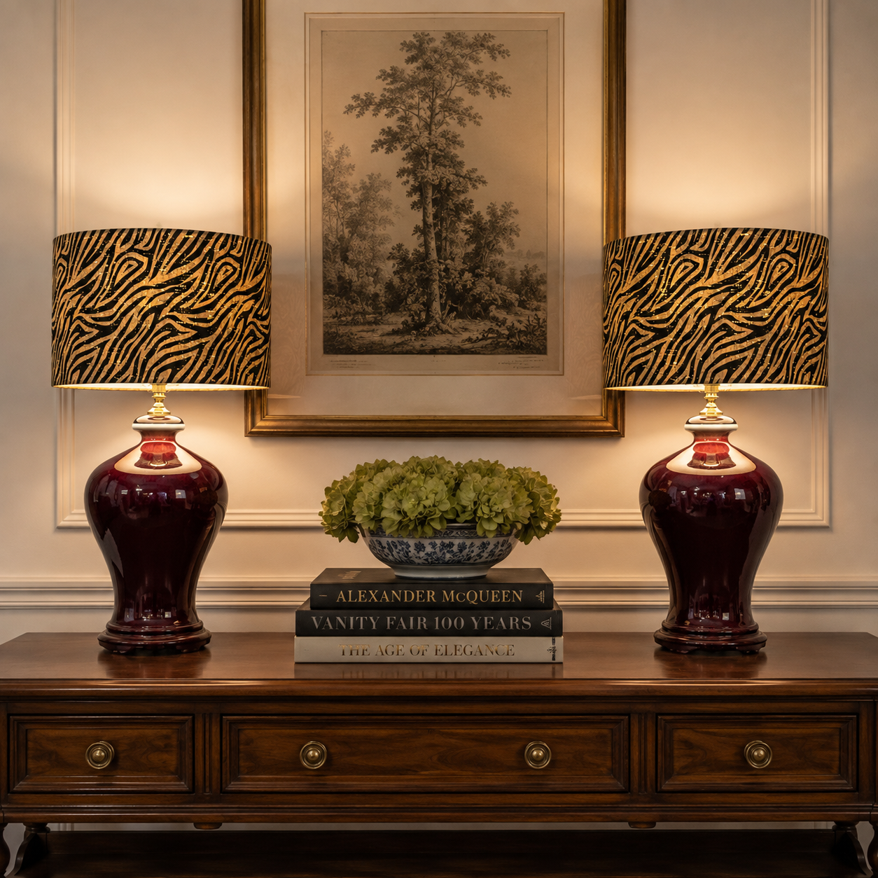 Two matching table lamps with deep burgundy glossy ceramic bases and black-and-gold zebra-patterned drum shades, placed on a wooden console table in a styled interior setting.