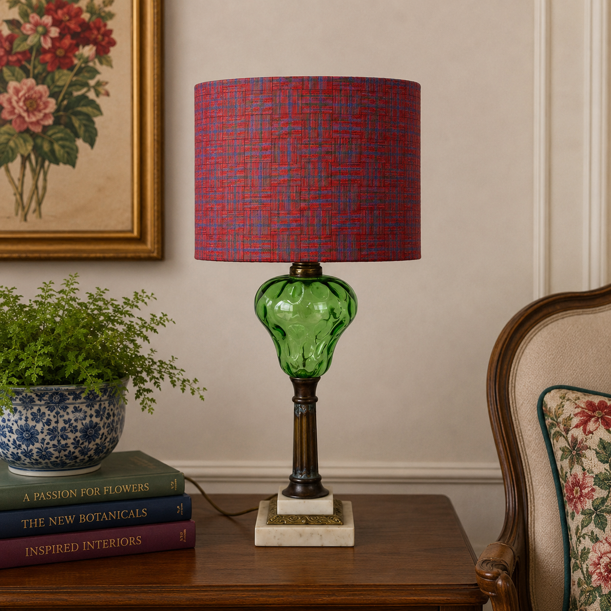 A table lamp with a textured red and blue patterned drum shade, a green glass bulb, and a dark metal stem on a marble base, styled on a wooden side table in a room setting.