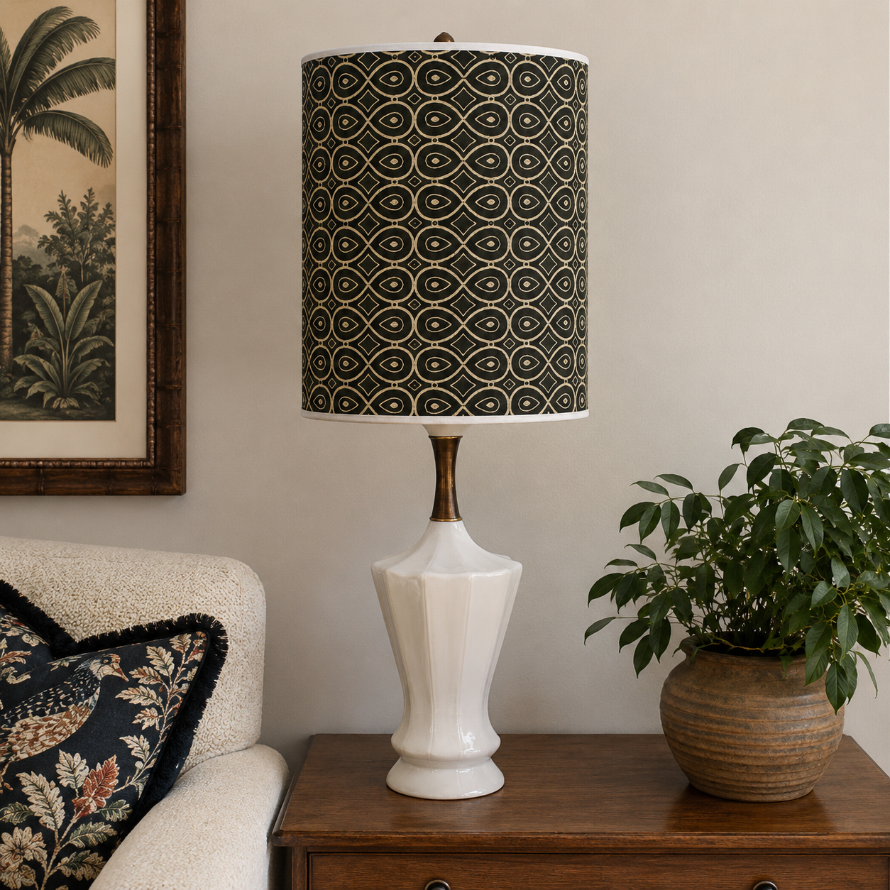 A table lamp with a white fluted ceramic base and a black drum shade featuring a repeating gold geometric pattern, styled on a wooden side table in a living room setting.