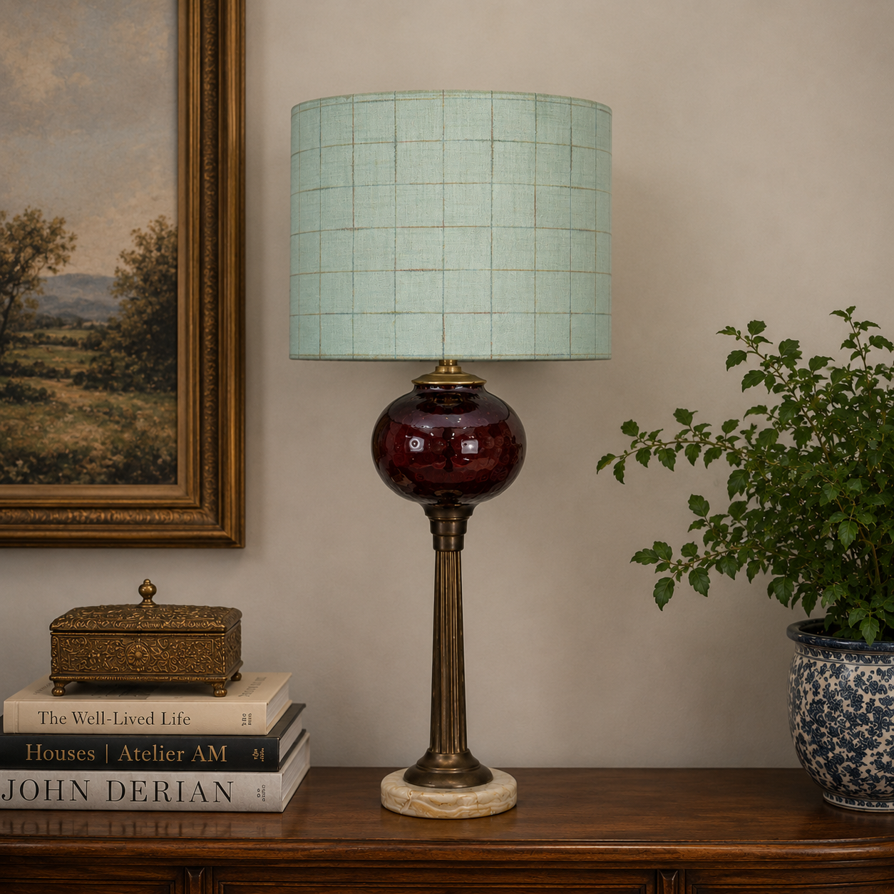 A table lamp with a light mint green checkered drum shade, a glossy dark red glass bulb, and a bronze-toned metal stem and base, displayed on a wooden console table in a styled room setting.